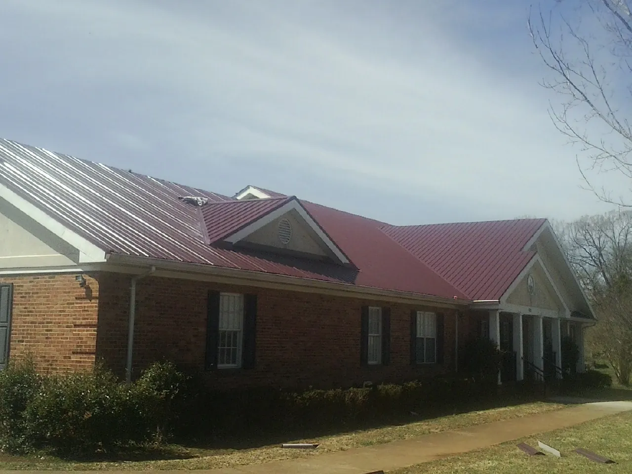 Red metal roof with gabled entries on a long brick building, from a Hail Damage Roof Repair job in Munds Park