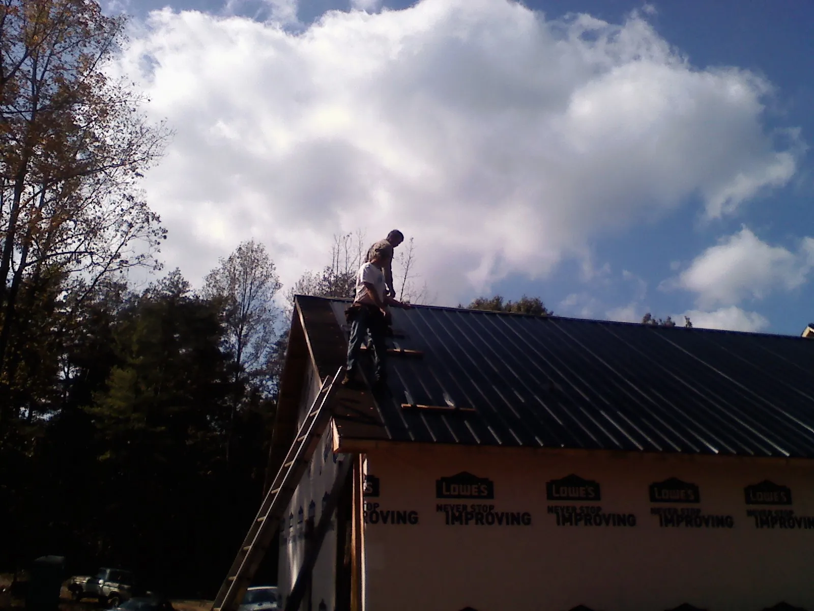 Roofer fastening dark metal panels high against a cloudy sky, from a Roof Inspection job in Munds Park