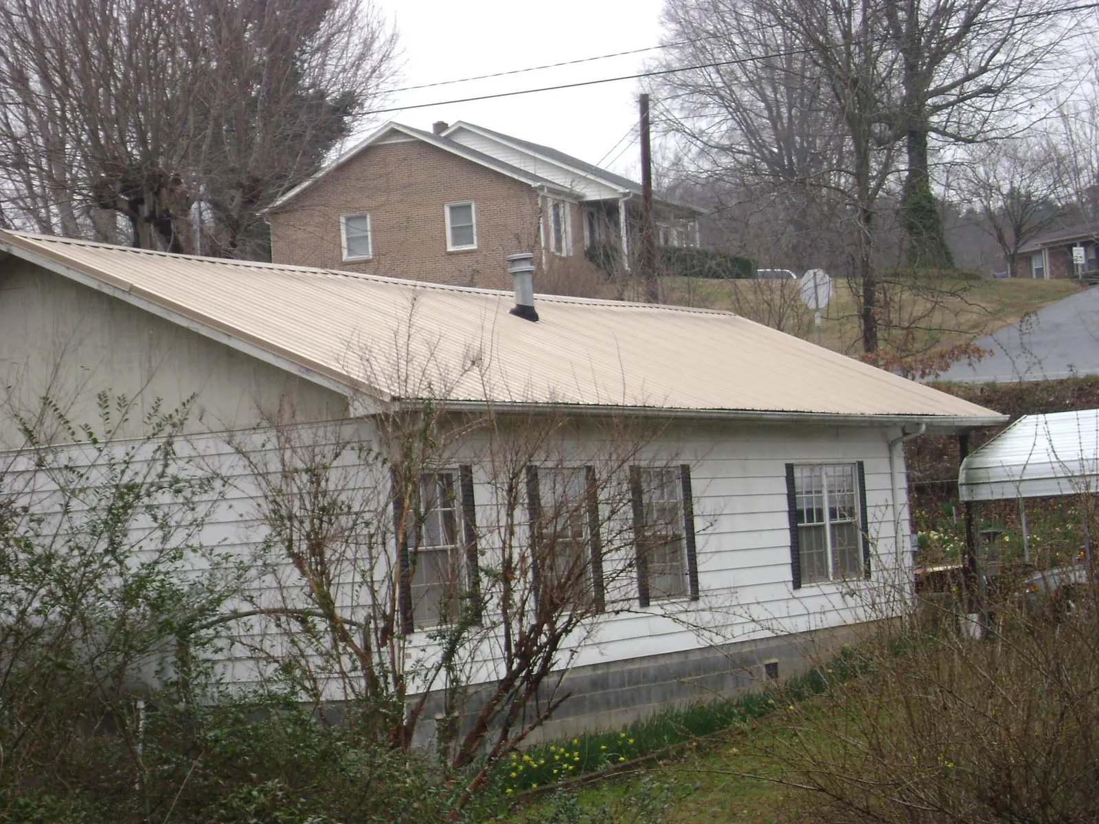 Tan metal roof on a white sided house set into a hillside — Commercial Roofing by Roofing Brothers in Munds Park